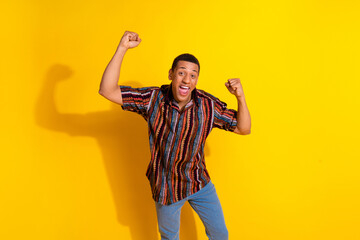 Naklejka premium Young man celebrating with joy against a vibrant yellow background while wearing a colorful casual shirt and denim jeans