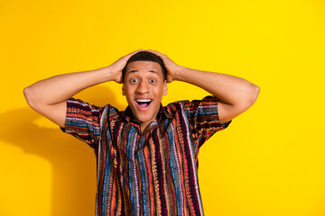 Excited young man with vibrant shirt holds head in cheerful pose against bright yellow background