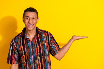 Young man in a colorful shirt showcasing a bright smile while gesturing with his hand against a...