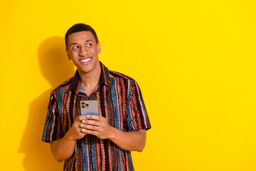 Young cheerful man holding a smartphone, smiling with a stylish dress against a bright yellow...