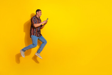 Young stylish man using smartphone against a vibrant yellow background expressing happiness and energy