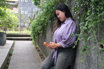 young Asian woman plays a kalimba while relaxing in a green city park during summer. The bright sunlight, lush surroundings, and soft melodies create a calm and refreshing outdoor scene