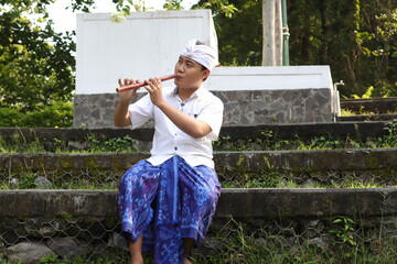 Portrait of Balinese Asian man playing traditional bamboo flute in outdoor park