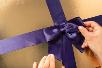 Elegant gold gift box adorned with a rich purple ribbon and bow. Perfect for special occasions.
