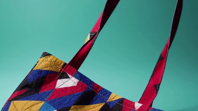 Close-up of handmade patchwork tote bag with colorful geometric pattern on turquoise background, sustainable fashion accessory