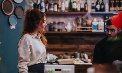 Two chefs appear in a cozy bar kitchen, engaged in culinary preparation amidst a stylish background featuring bottles and kitchenware, evoking an atmosphere of creativity, warmth, and collaboration.