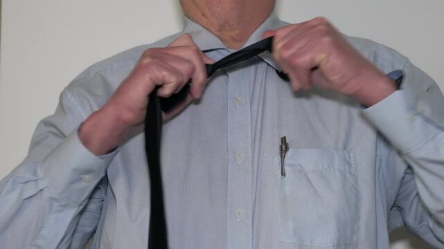 Business man in shirt and black tie is taking his tie off, and opens the upper button of his shirt, to get some relief. 