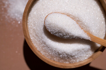 White granulated sugar in wooden spoon and bowl on brown background top view close-up. Concept of eating sweets, health and diabetes issue, sugar-free diet