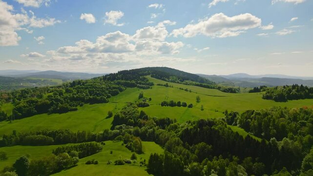 Aerial summer flight over lush green meadows and forests near Jested mountain with distant view of Jizera Mountains and picturesque villages scattered across the landscape