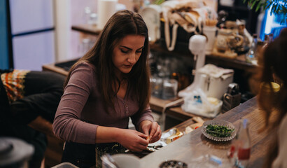 A young woman diligently prepares food ingredients at a lounge bar counter, surrounded by utensils and fresh herbs. The environment reflects a cozy and productive setting for culinary tasks.