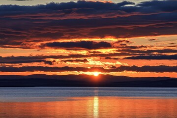 Fototapeta premium Dramatic sunset over water with mountains in the distance and colorful clouds in the sky scenic view