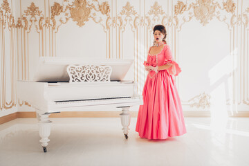 Elegant young woman in a classic pink gown standing by a white piano
