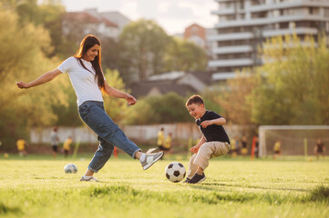 Obraz premium Active time spending with soccer ball. Mother and son are together on the summer field
