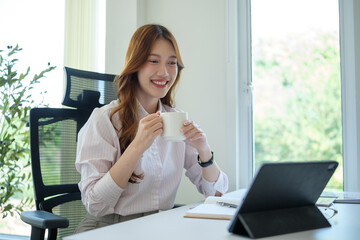 Confident woman multitasking with digital work and relaxation in a bright office space.