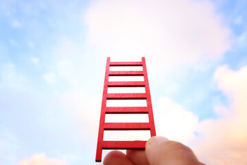 Hand holding red ladder in front of sky. Concept of aiming high and achieving success