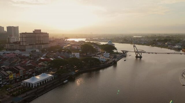 Dramatic golden hour aerial view of the Darul Hana Bridge, Sarawak River, and Kuching State Mosque, with the warm sunlight blanketing the cityscape.