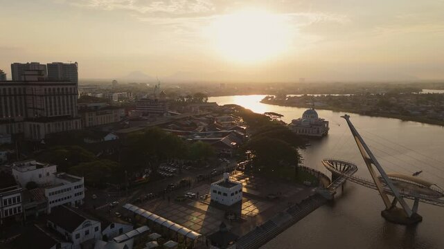 Aerial drone image of Kuching&rsquo;s Darul Hana Bridge stretching over the Sarawak River during golden hour. The State Mosque and historic buildings surrounding the waterfront.