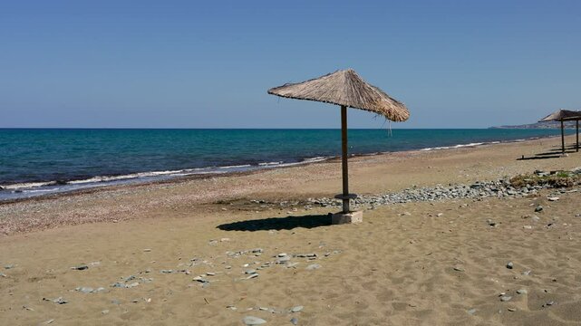  Serene coastal view with rows of thatched beach umbrellas at Argaka Beach, Cyprus.  Calm sea glistens in  background