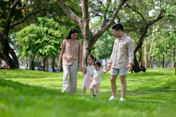Obraz premium Happy family walking together in a sunny green park, each parent carrying a child.