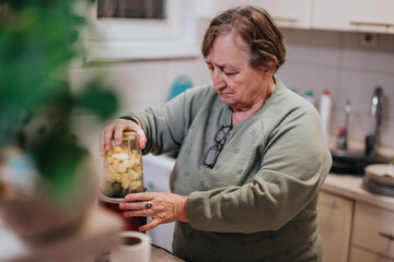 A senior woman preparing a nutritious drink by blending fruits and vegetables using a blender in a cozy kitchen, reflecting a healthy and proactive lifestyle.