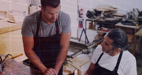 Image of financial graphs over caucasian men working in carpentry workshop