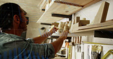 Image of financial graphs over caucasian man searching for tools in carpentry workshop