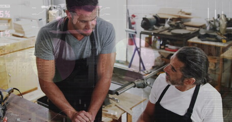 Image of financial graphs over caucasian men working in carpentry workshop