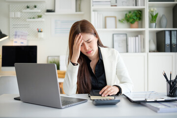 Businesswoman feeling stressed while working on financial reports at the office, holding her head...