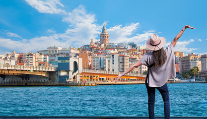 Happy woman in hat open arms in free happiness standing and posing - Galata Tower, Galata Bridge, Karakoy district and Golden Horn at morning - istanbul, Turkey