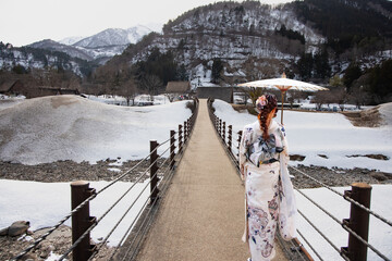 Japanese woman holding an umbrella and wearing a traditional japanese kimono - The Historic Villages of Shirakawa with suspension bridge in winter - Japan