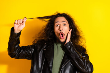 Young man in leather jacket with long hair expressing surprise and playfulness against a vibrant yellow background