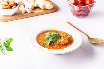 Fresh aromatic hot Thai soup Tom Yum with mushrooms, shrimps and different spices on white marble background close up. Tasty food concept.