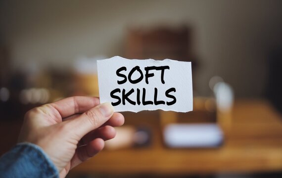 A hand holding a piece of white paper with the text soft skills written on it