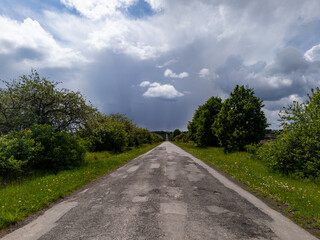 A dirt road in the middle of a grassy field under a cloudy sky