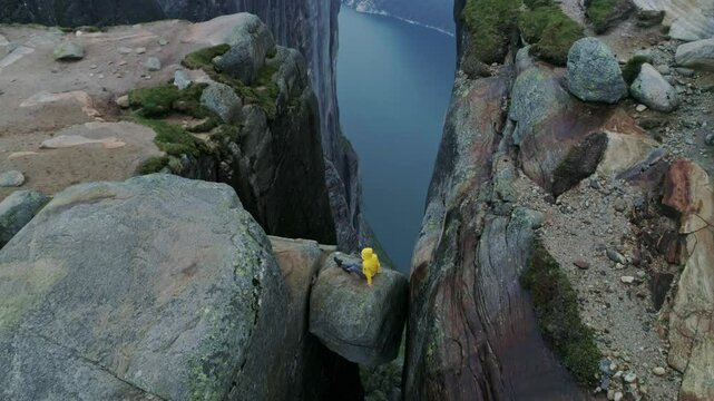 Solo traveler in yellow jacket balanced on boulder wedged between high cliffs