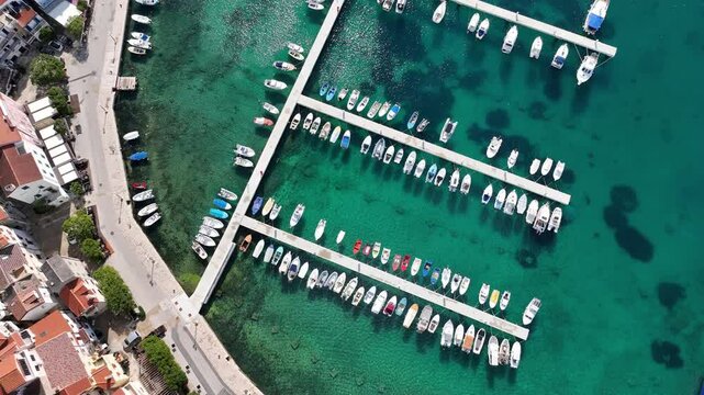 Baska beach and coastline with crystal-clear turquoise water, marina boats, city street, sunny summer mood captured from drone view on Krk Island. Baska vacations town in Adriatic sea