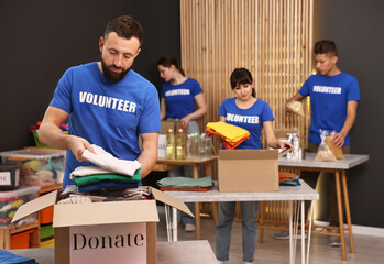 Group of volunteers packing donation goods at tables indoors, selective focus