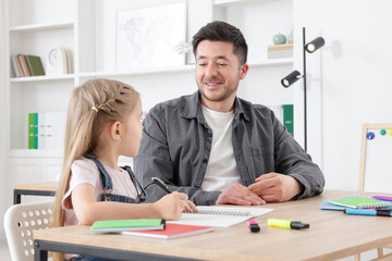 Teacher having lesson with little girl at desk indoors