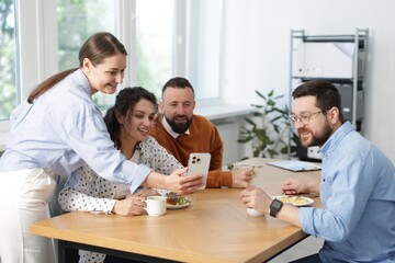 Woman showing her colleagues something on smartphone during lunch break in office
