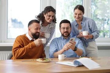 Man showing his colleagues something on smartphone during lunch break in office