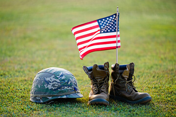 American flag displayed beside military boots and helmet on green grass outdoors