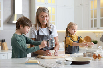 Grandmother and her grandchildren making dough at white marble table in kitchen