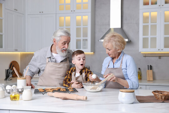 Grandparents and their grandson cooking together at white marble table in kitchen