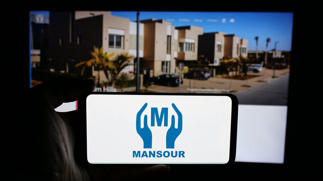 Stuttgart, Germany - 05-02-2025: Person holding cellphone with logo of Egyptian company Mansour Group on screen in front of webpage. Focus on phone display.