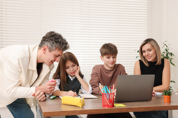 Parents and their children doing homework with laptop at table indoors