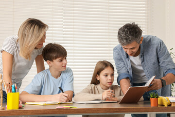 Parents and their children doing homework with laptop at table indoors