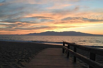 Sunset over the ocean, a wooden boardwalk leads to the shore
