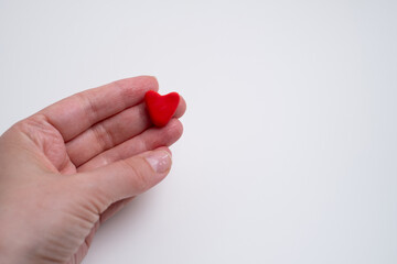 Woman with red heart on light background. Health, medicine and charity concept - close-up of female hands with small red heart