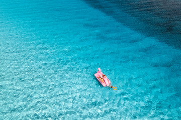 Aerial view of Inflatable pink flamingo with people on crystal clear blue water on summer sunny day. Top drone view of relax family on boat, azure sea in Sardinia Island, Italy. Travel and vacation