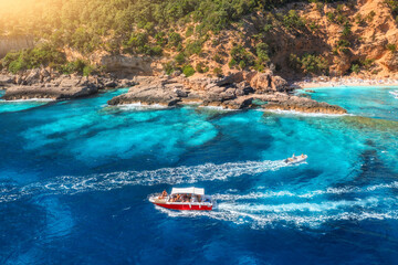 Aerial view of speed boat and sandy beach with people on sunny summer day. Top drone view of motorboat, green trees, rocks, sea coast. Mediterranean sea. Travel in Sardinia island, Italy. Tropical